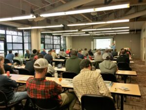 Pesticide school attendees are seated at tables taking notes as Dr. Wayne Buhler teaches.